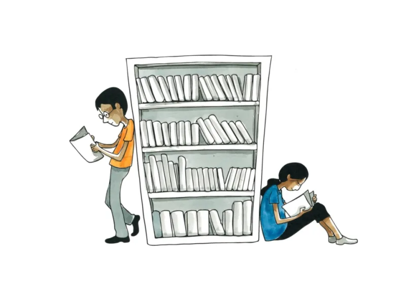 Two students reading beside a library bookshelf